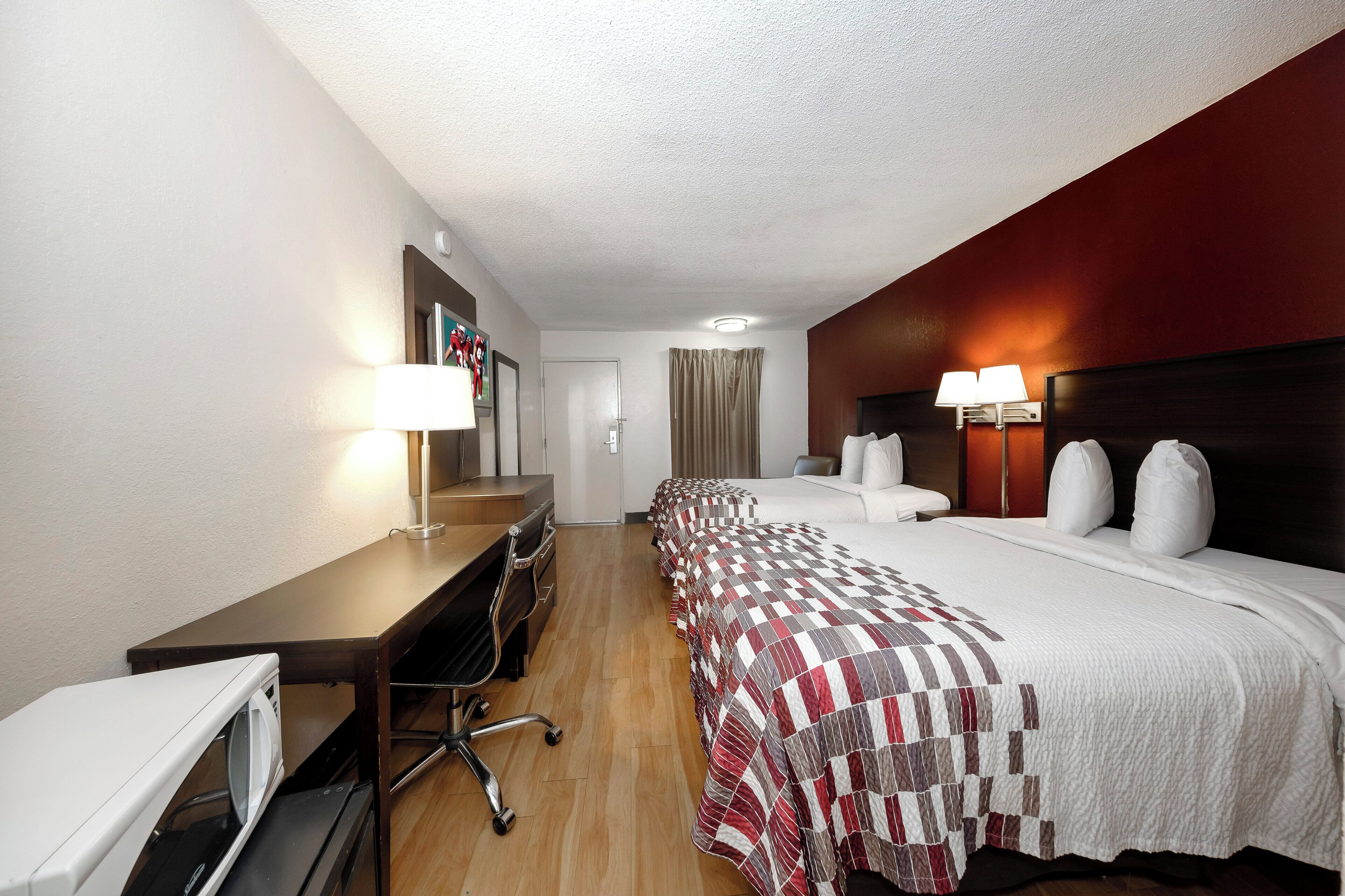 Een hotelkamer met een bureau, twee bedden, een hoofdeinde met lampen en een magnetron.