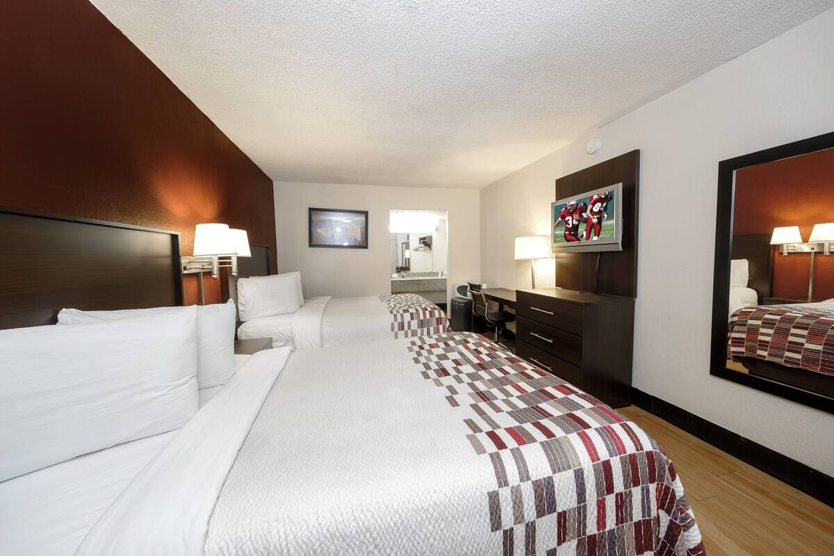 A hotel room with a large bed, a desk, a chair, a TV, and a mirror.
