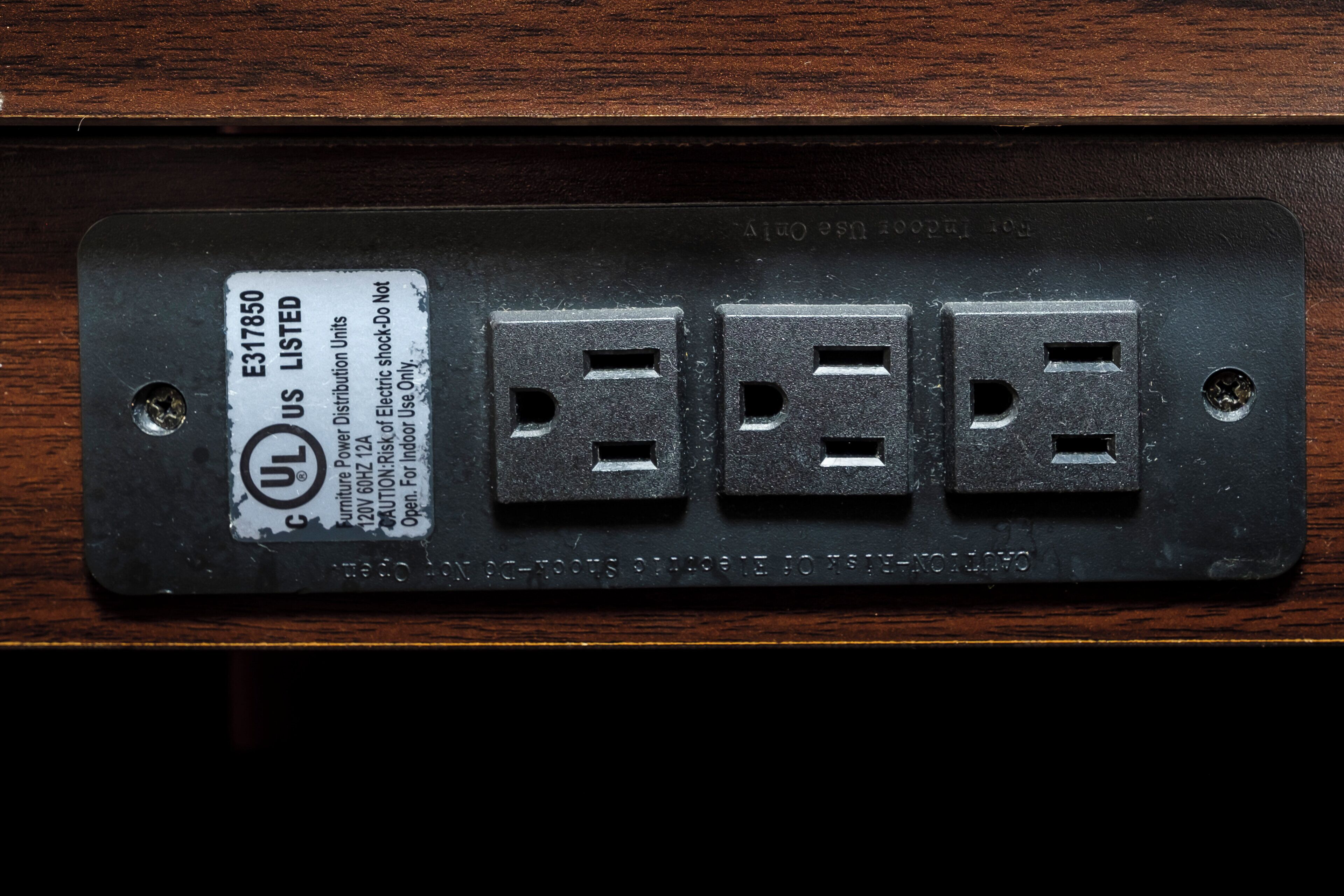 A black electrical outlet with four sockets, a label indicating it is UL listed, and a warning about indoor use only.