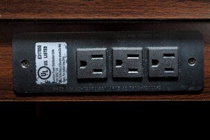 Un enchufe eléctrico negro con cuatro tomas, una etiqueta que indica que cuenta con la certificación UL, y una advertencia sobre uso exclusivo en interiores.