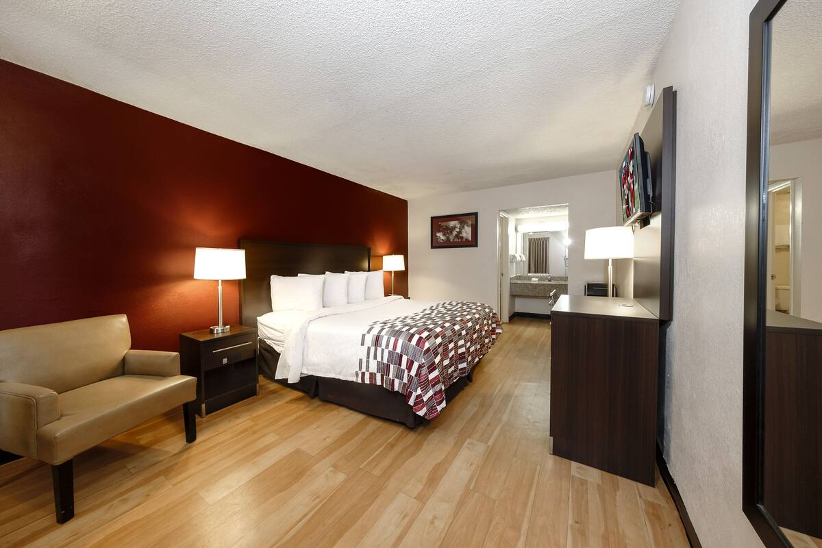 A hotel room with a bed, a sofa, a nightstand, a desk, and a mirror.