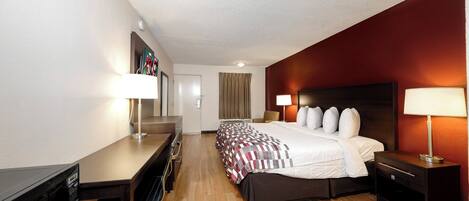 A hotel room with a bed, bedside tables, a desk, a chair, and a television.
