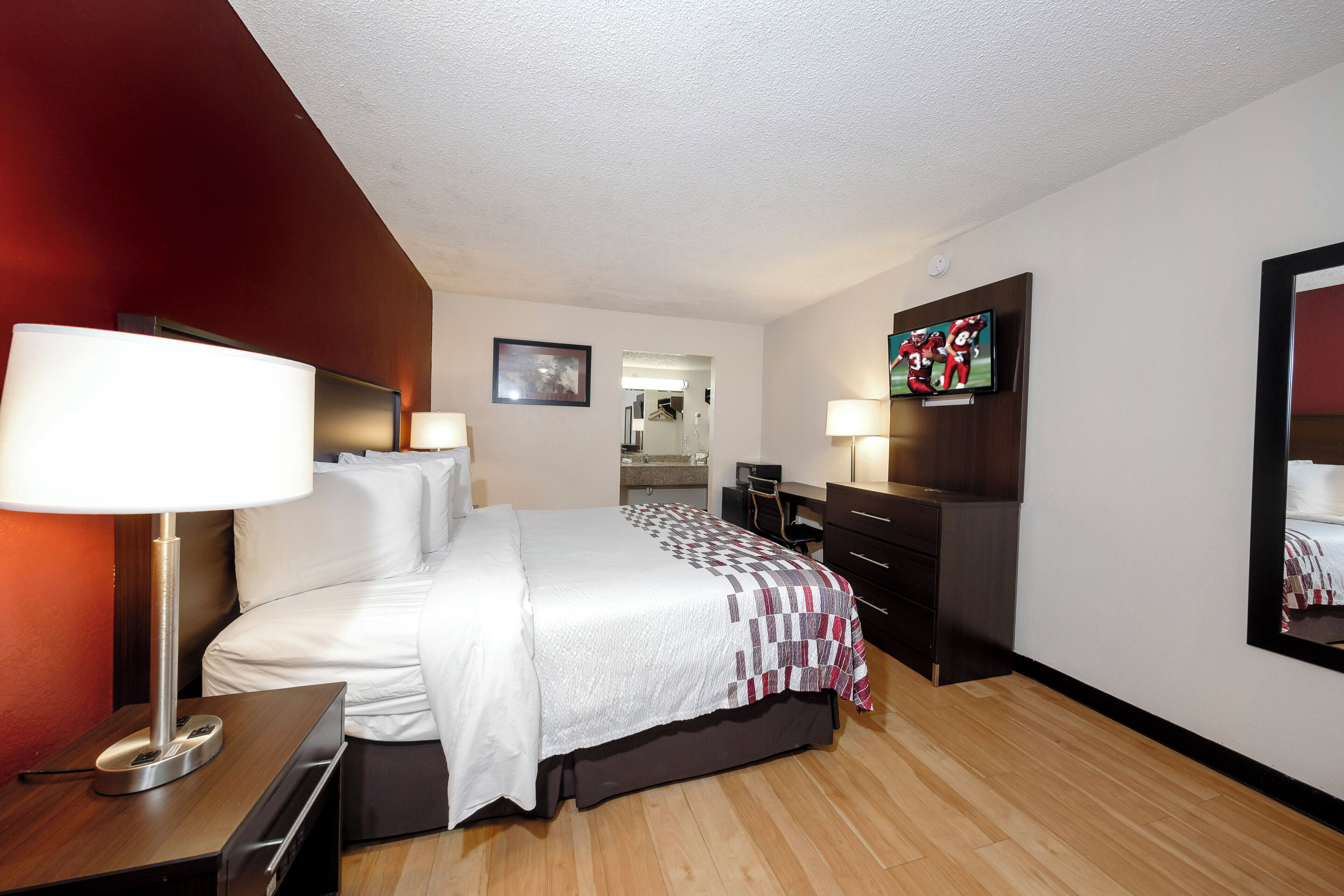 A hotel room with a bed, bedside lamps, a television, a desk with a lamp, and a mirror.