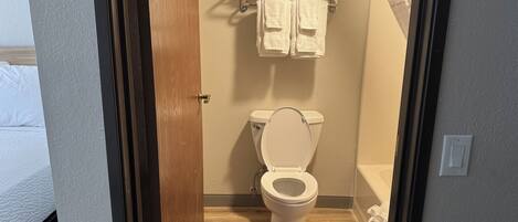 A bathroom with a toilet, a towel rack with towels, and a wooden floor.
