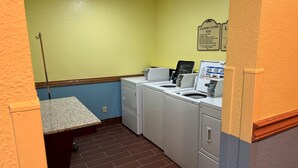 Uma lavanderia com duas máquinas de lavar, uma secadora e uma pequena mesa com um monitor de computador.