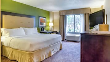 A hotel room with a large bed, a desk with a television, a lamp, and a window with curtains.