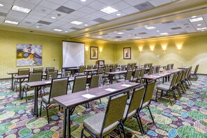 A conference room with multiple tables and chairs, a projector screen, and a large painting on the wall.
