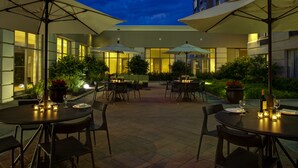 An outdoor dining area with tables, chairs, and umbrellas. - Holiday Inn Indianapolis Carmel by IHG (Indianapolis)