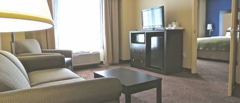 A hotel room with a sofa, a small table, a television, and a bed.