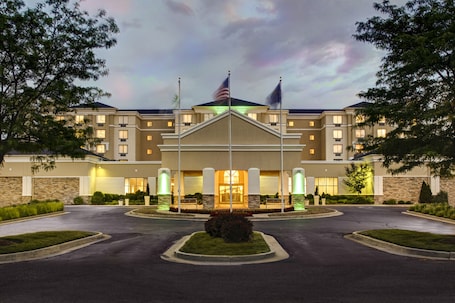 A hotel with a central entrance, flagpoles, and a landscaped driveway.