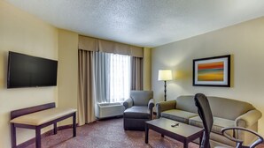 A hotel room with a flat-screen TV, a sofa, a chair, a bench, a coffee table, and a lamp. - Holiday Inn Indianapolis Carmel by IHG (Indianapolis)