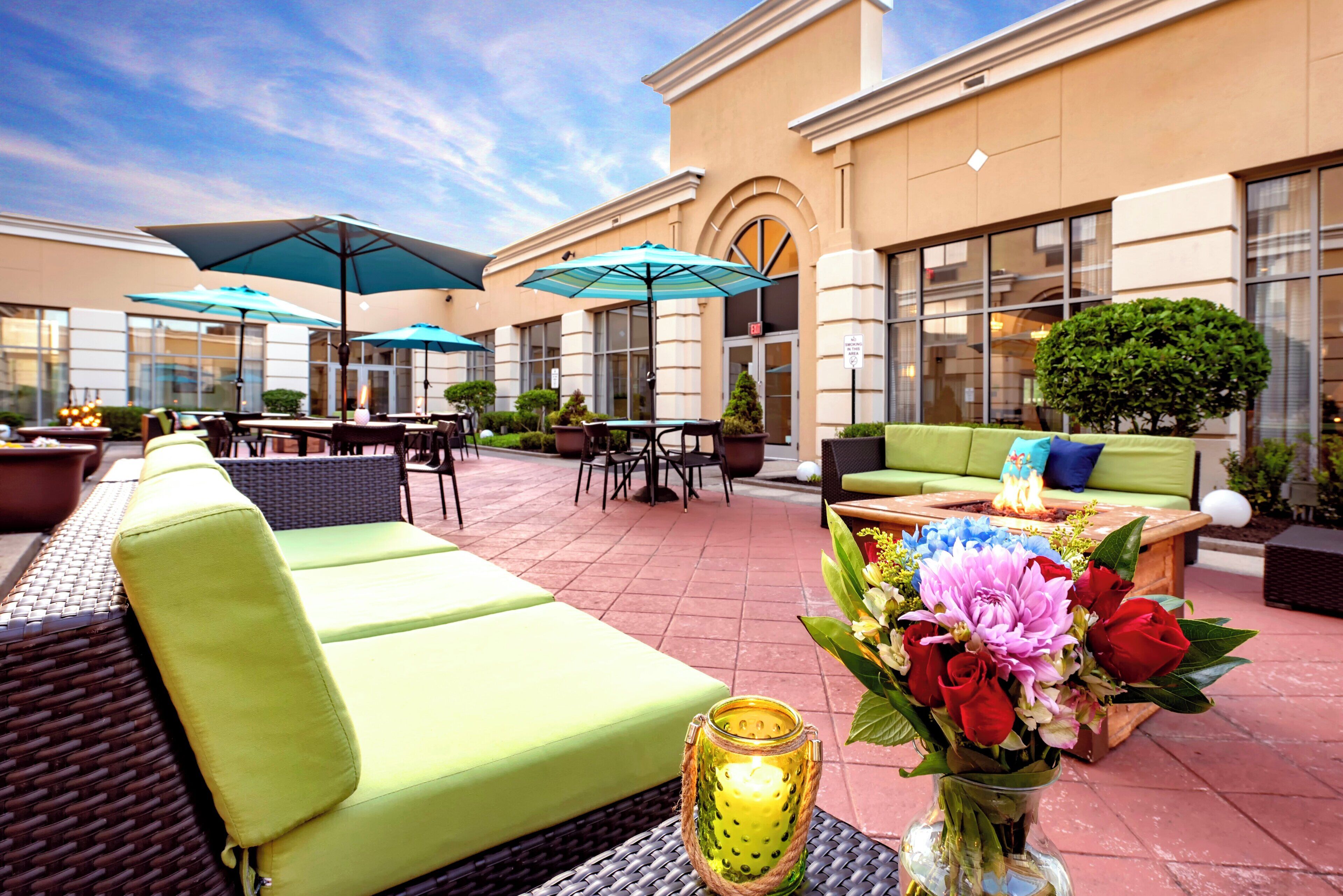 An outdoor seating area with green sofas, umbrellas, and a table with a candle and flowers.