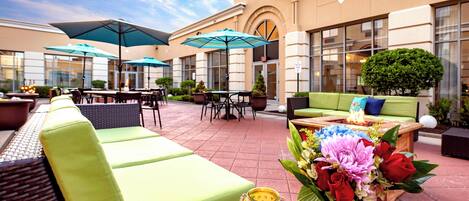 An outdoor seating area with green sofas, umbrellas, and a table with a candle and flowers.