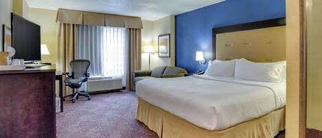 A hotel room with a large bed, a desk with a computer, a chair, and a television.