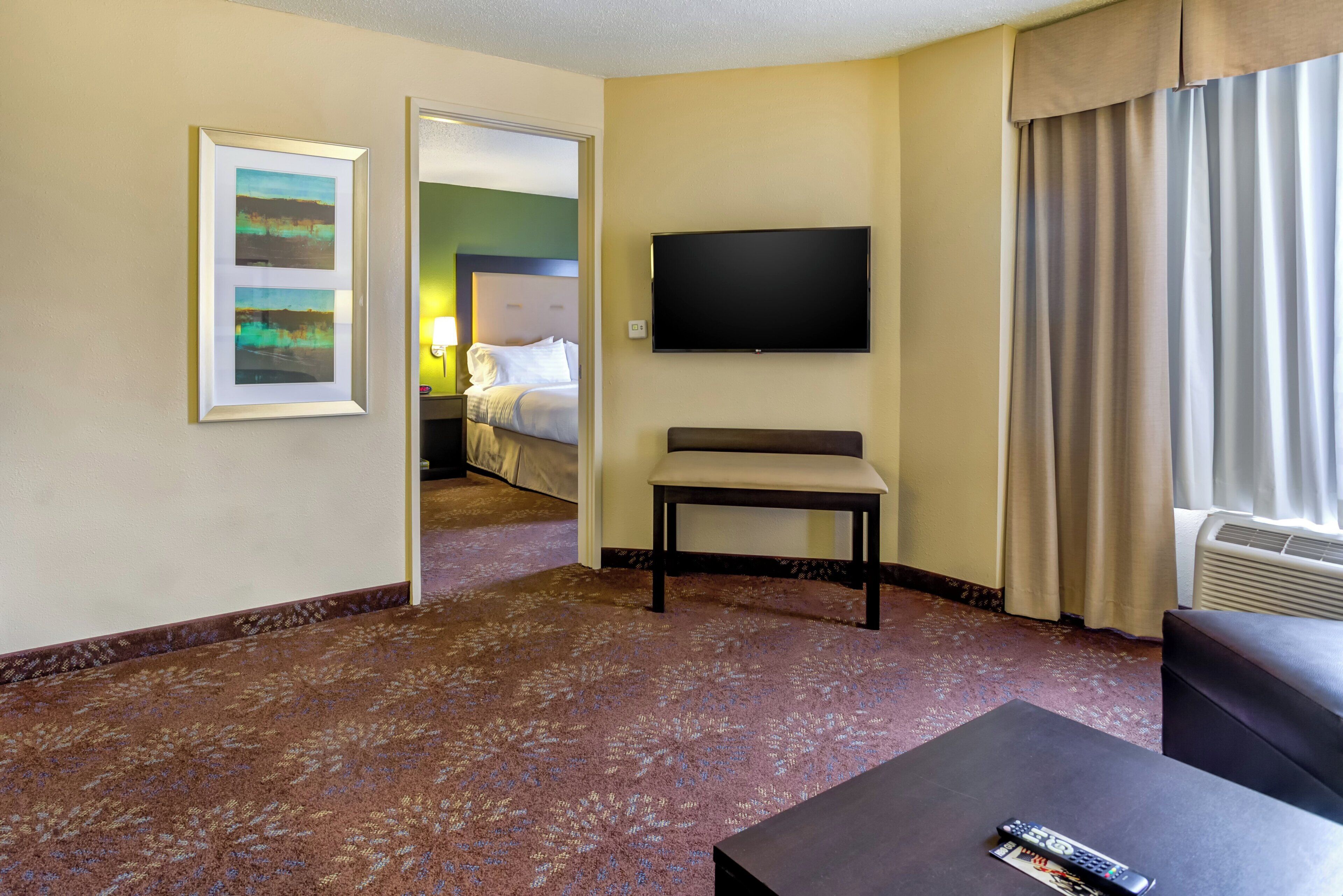 A hotel room with a bed, a television, a chair, and a carpeted floor.