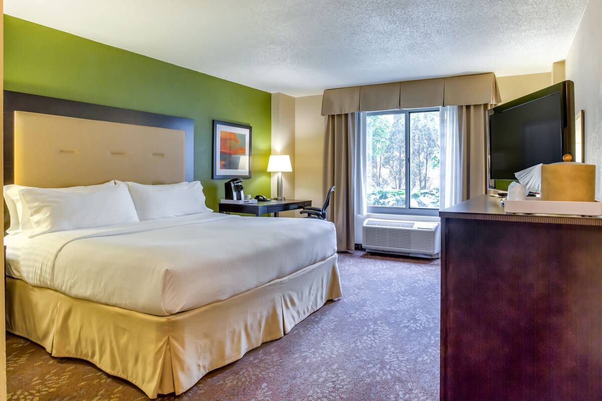 A hotel room with a large bed, a desk, a television, and a window with curtains.