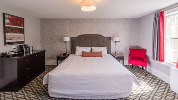 Une chambre d’hôtel avec un grand lit, une commode, deux tables de chevet, un fauteuil rouge et une fenêtre avec des rideaux.