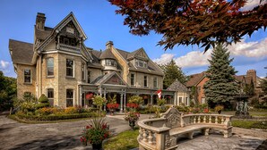 A large, historic house with a prominent front porch, a stone staircase, and a well-maintained garden with various plants and flowers.