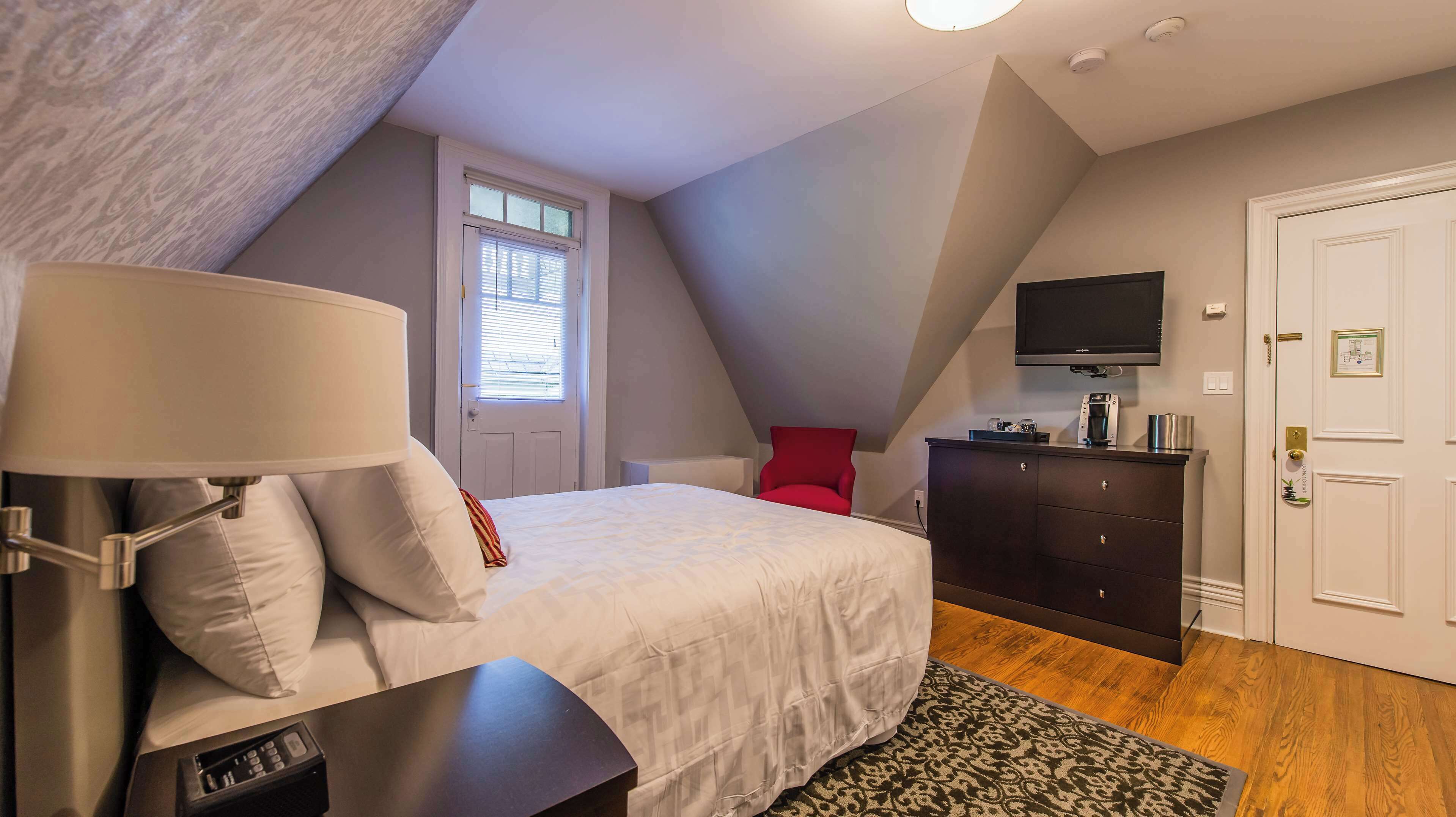 Ein Schlafzimmer mit Bett, Schreibtisch, Stuhl, Kommode, Fernseher und einer Tür.