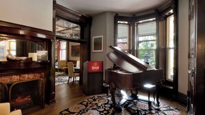 Un piano de cola en una habitación luminosa con chimenea, ventanas amplias y un tapete con motivos.