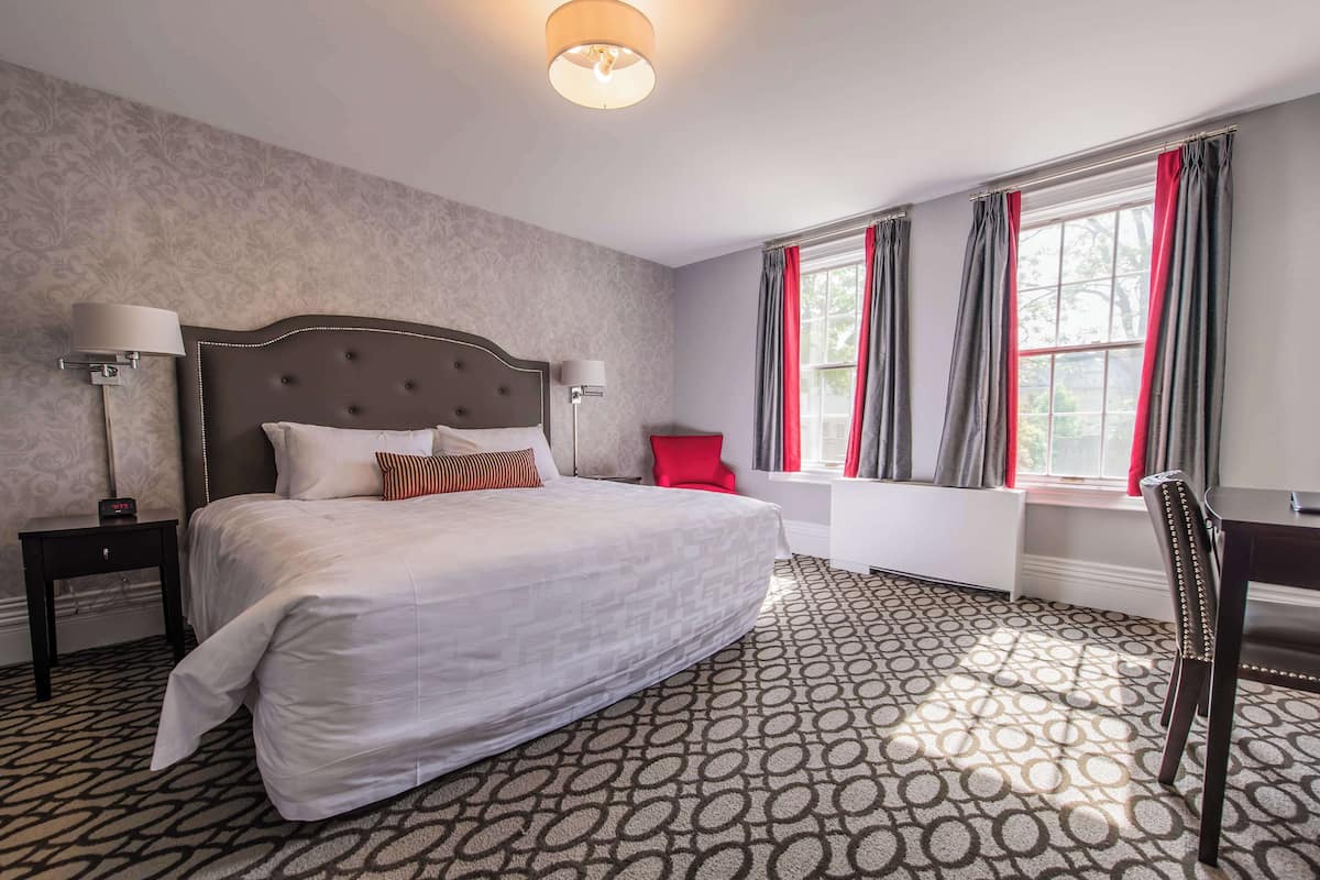 A hotel room with a large bed, two bedside lamps, a red chair, a desk, and a window with curtains.
