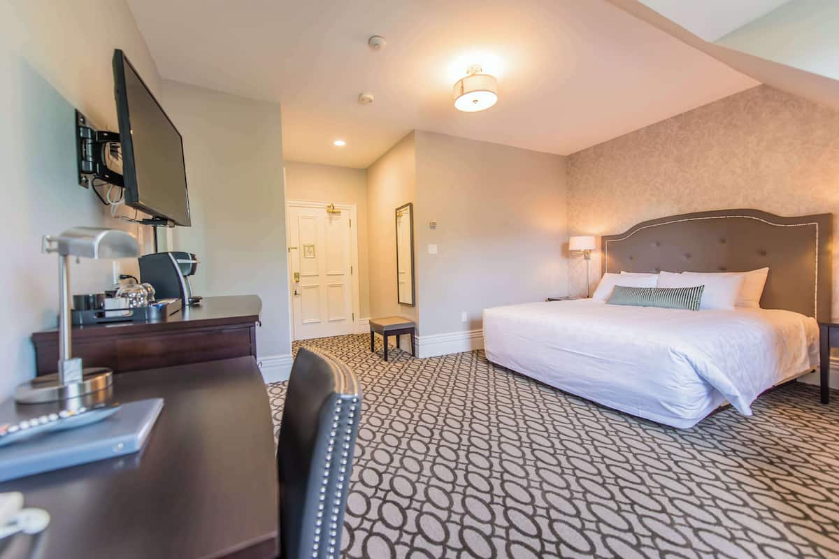 A hotel room with a bed, desk, chair, TV, and a door.