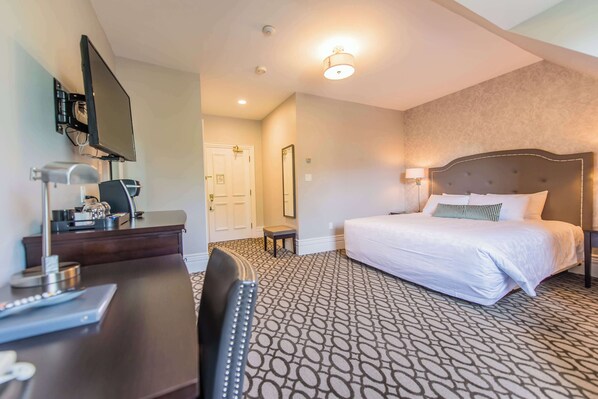 A hotel room with a bed, desk, chair, TV, and a door.