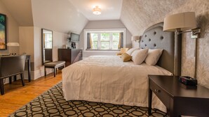 A bedroom with a large bed, a desk, a chair, a TV, and a window with curtains.