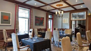 A dining area with tables set for four, wooden chairs, a chandelier, and artwork on the walls.
