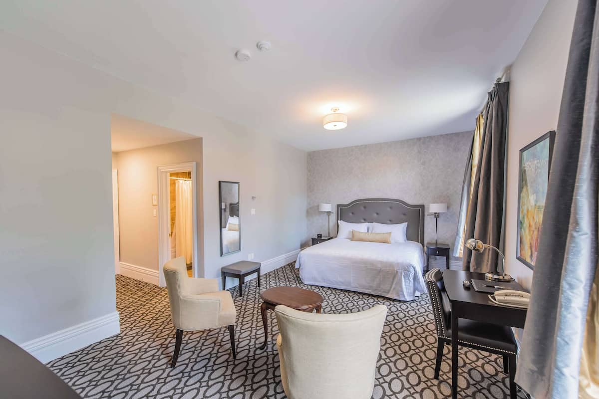 A hotel room with a bed, a desk, a chair, a small table, and a nightstand.