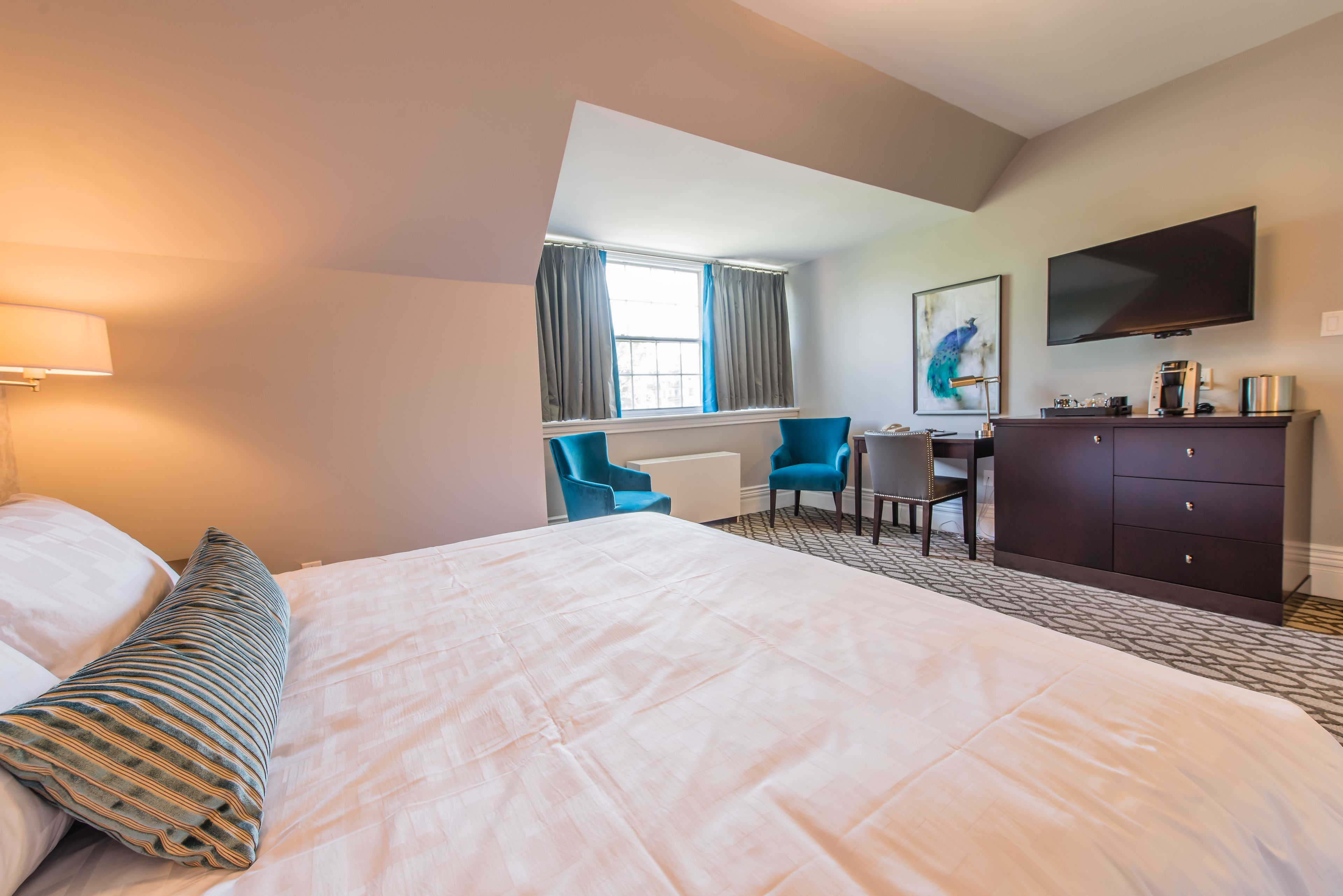 A hotel room with a large bed, a desk, a chair, a TV, and a window with curtains.