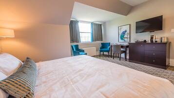 A hotel room with a large bed, a desk, a chair, a TV, and a window with curtains.