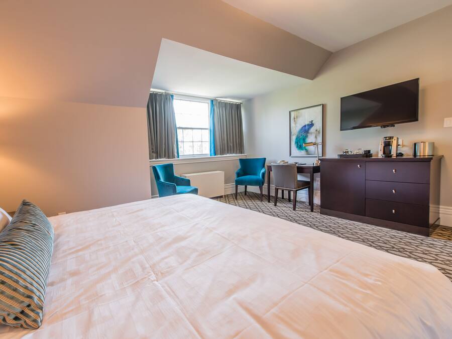 A hotel room with a large bed, a desk, a chair, a TV, and a window with curtains.