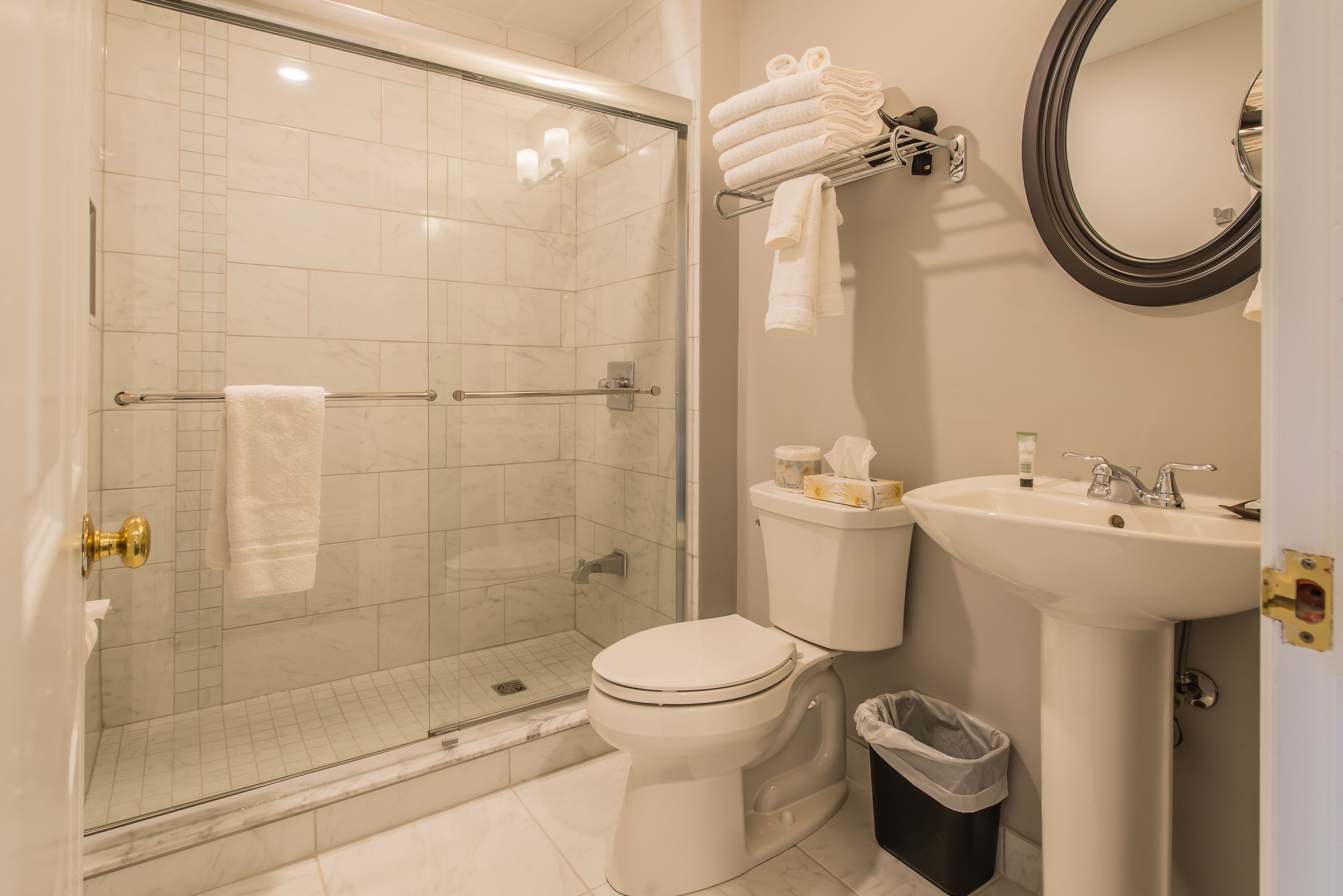 A bathroom with a glass-enclosed shower, a toilet, a sink, and a towel rack with folded towels.