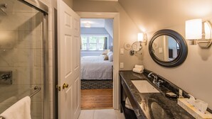A hotel bathroom with a glass shower, a sink with a marble countertop, and a large mirror.