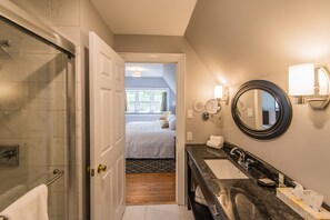 A hotel bathroom with a glass shower, a sink with a marble countertop, and a large mirror.
