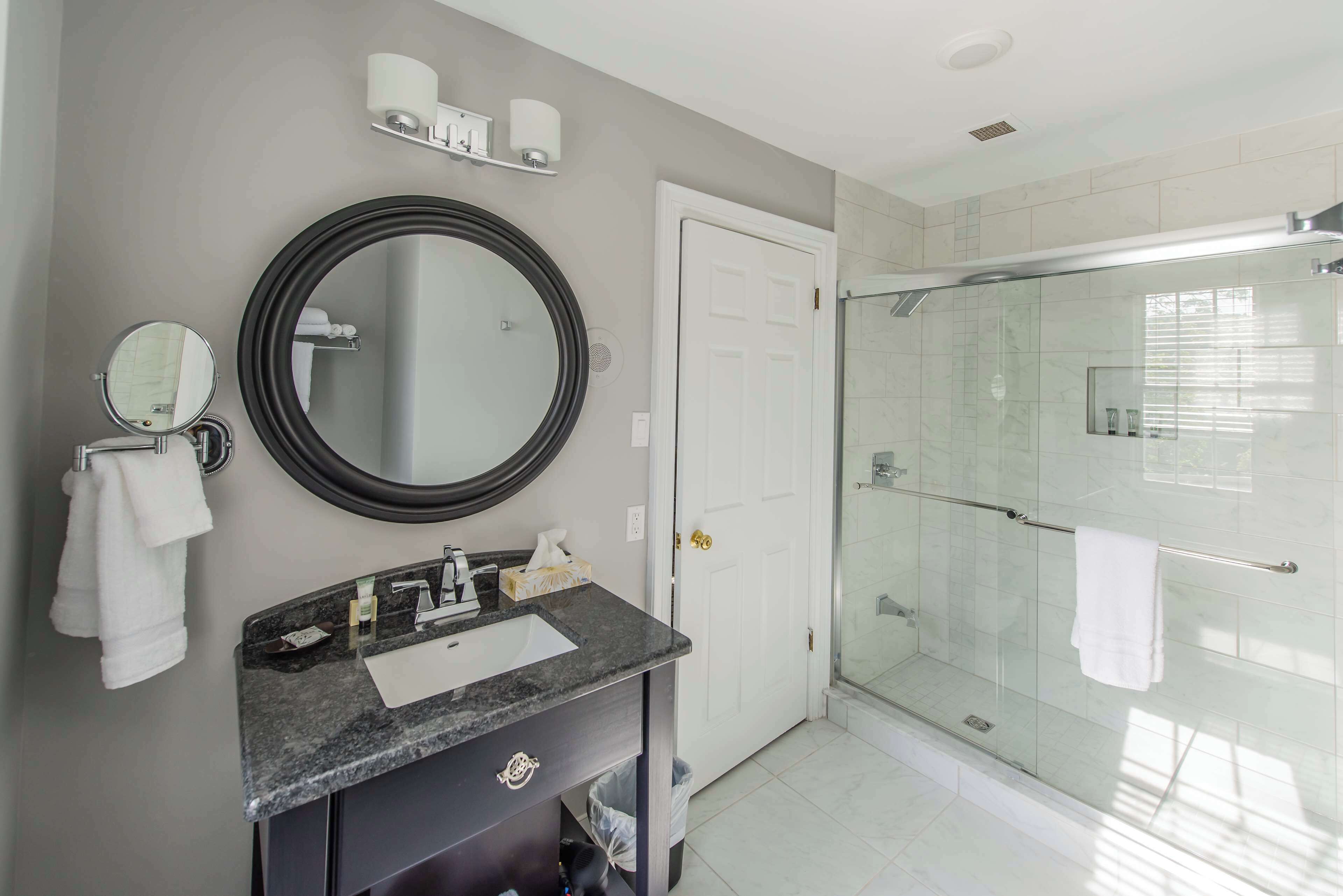 A modern bathroom with a large mirror, a sink, and a glass-enclosed shower.