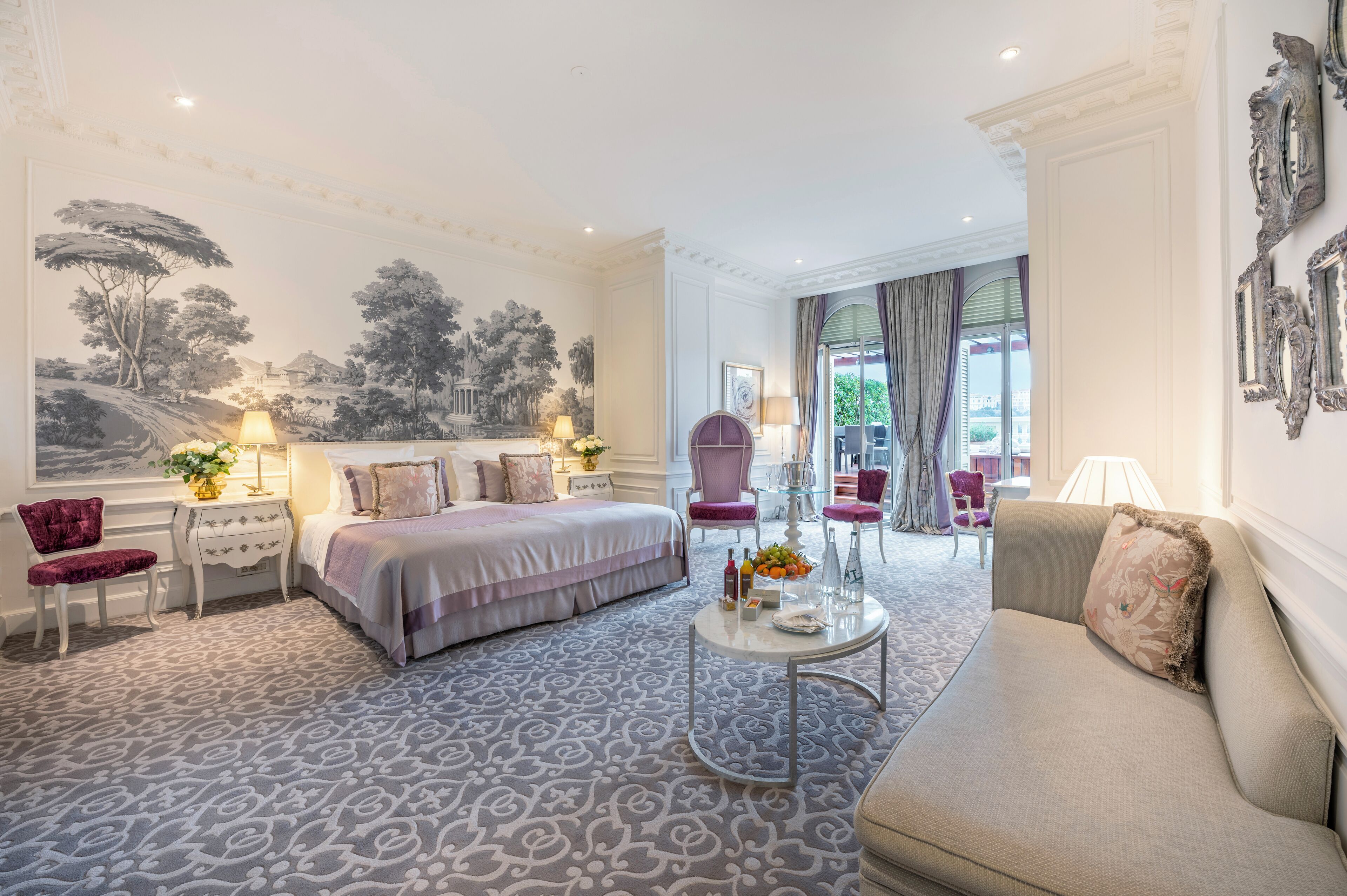 A hotel room with a bed, two armchairs, a sofa, a small table, and a large mural on the wall.