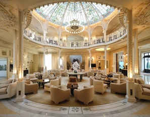A grand lobby with a high ceiling, ornate columns, and a central chandelier.