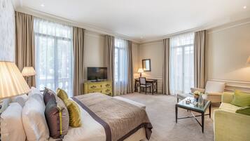 A hotel room with a bed, a desk, a television, and a seating area with a sofa and armchairs.