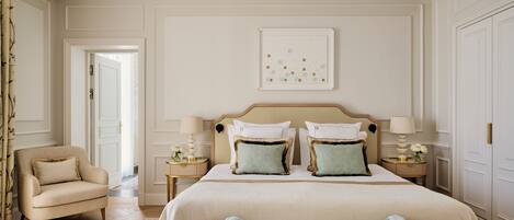 A bedroom with a large bed, two nightstands, a chair, and a framed picture on the wall.