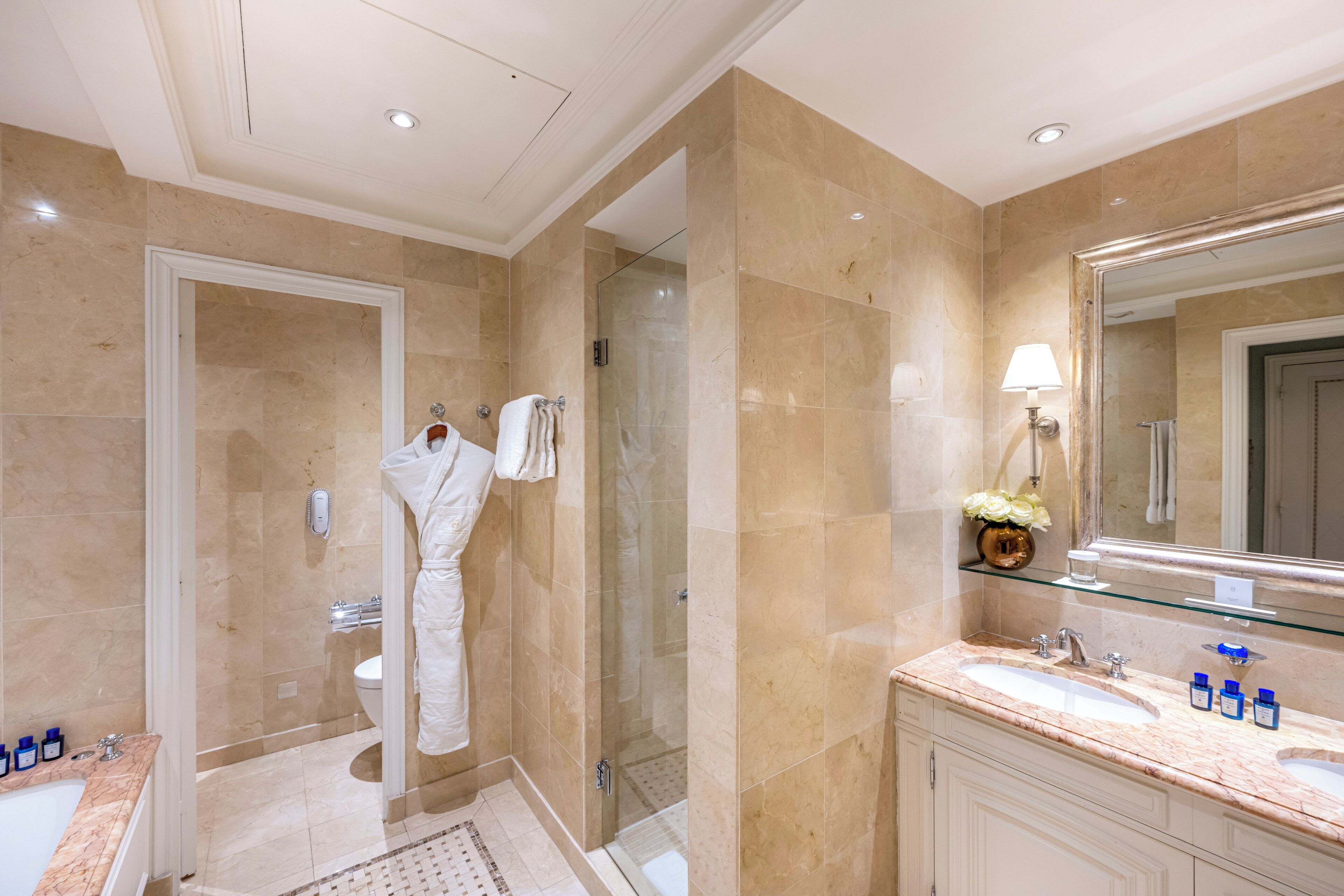A modern bathroom with a glass shower enclosure, a large mirror, and a marble countertop with two sinks.