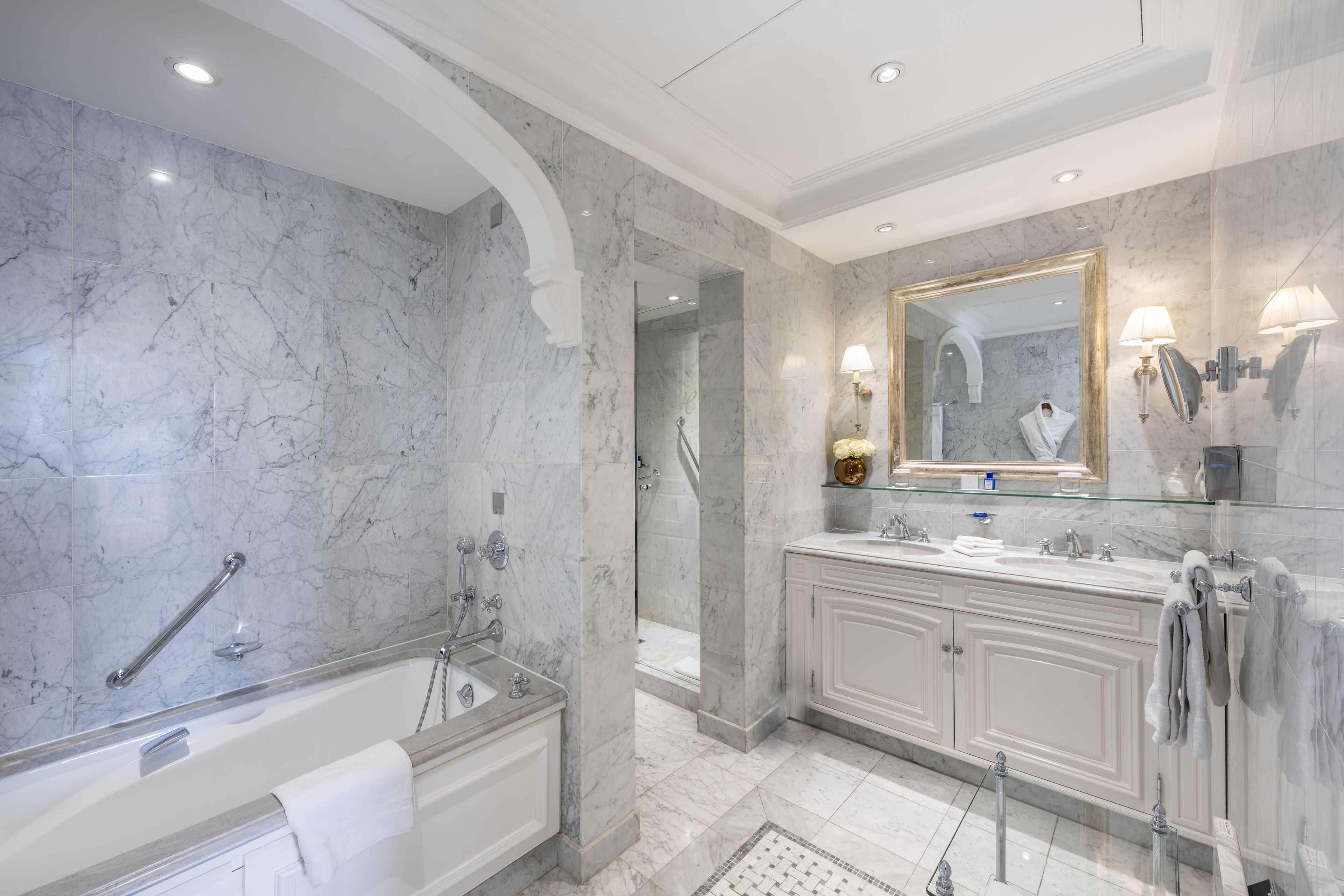 Une salle de bain moderne avec un mur en marbre, une baignoire sur pieds, un grand miroir et un meuble-lavabo doté d’un évier et d’un porte-serviettes.