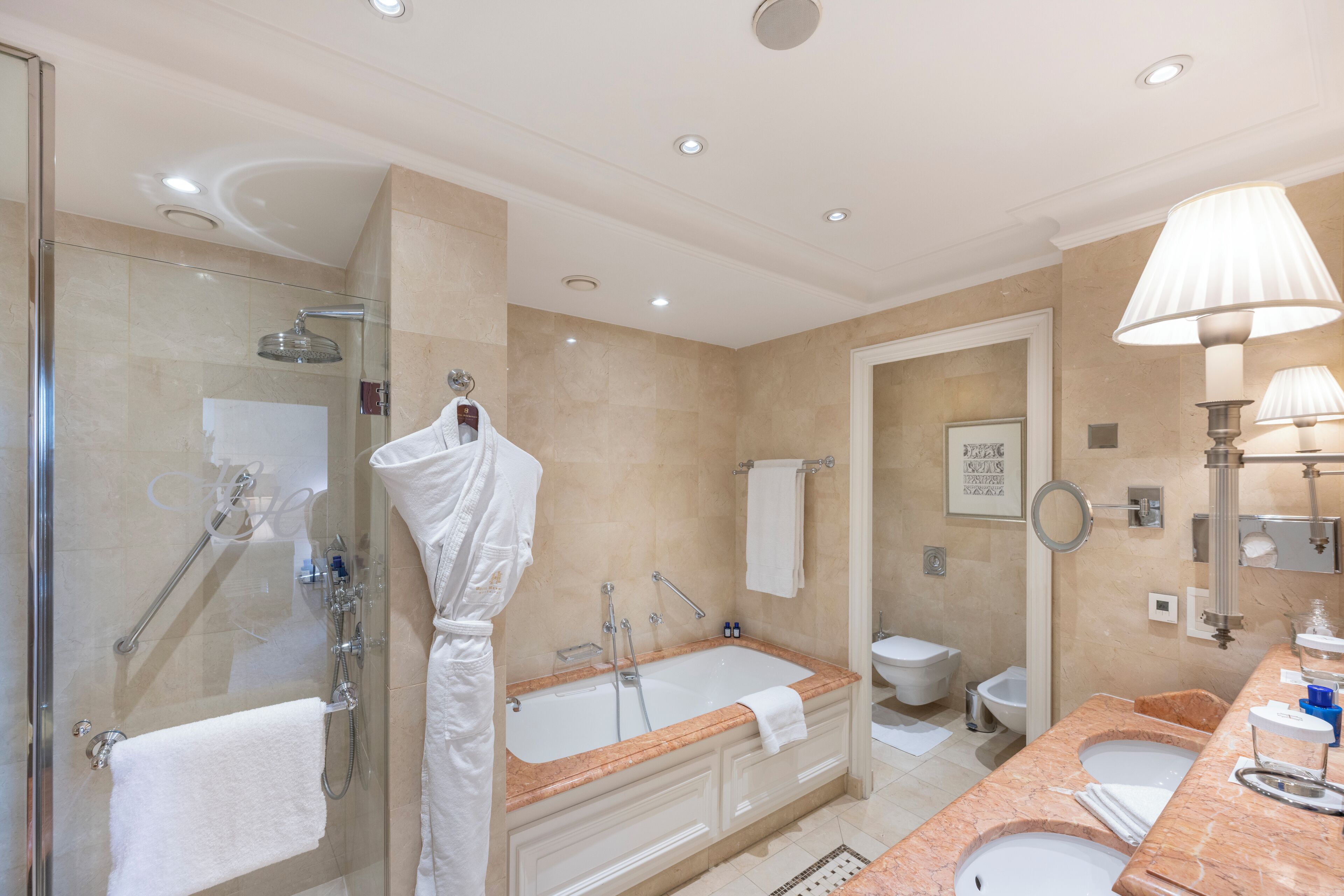 Un baño moderno con ducha envuelta en vidrio, una bañera independiente grande, un tocador con encimera de mármol y un inodoro de pared.