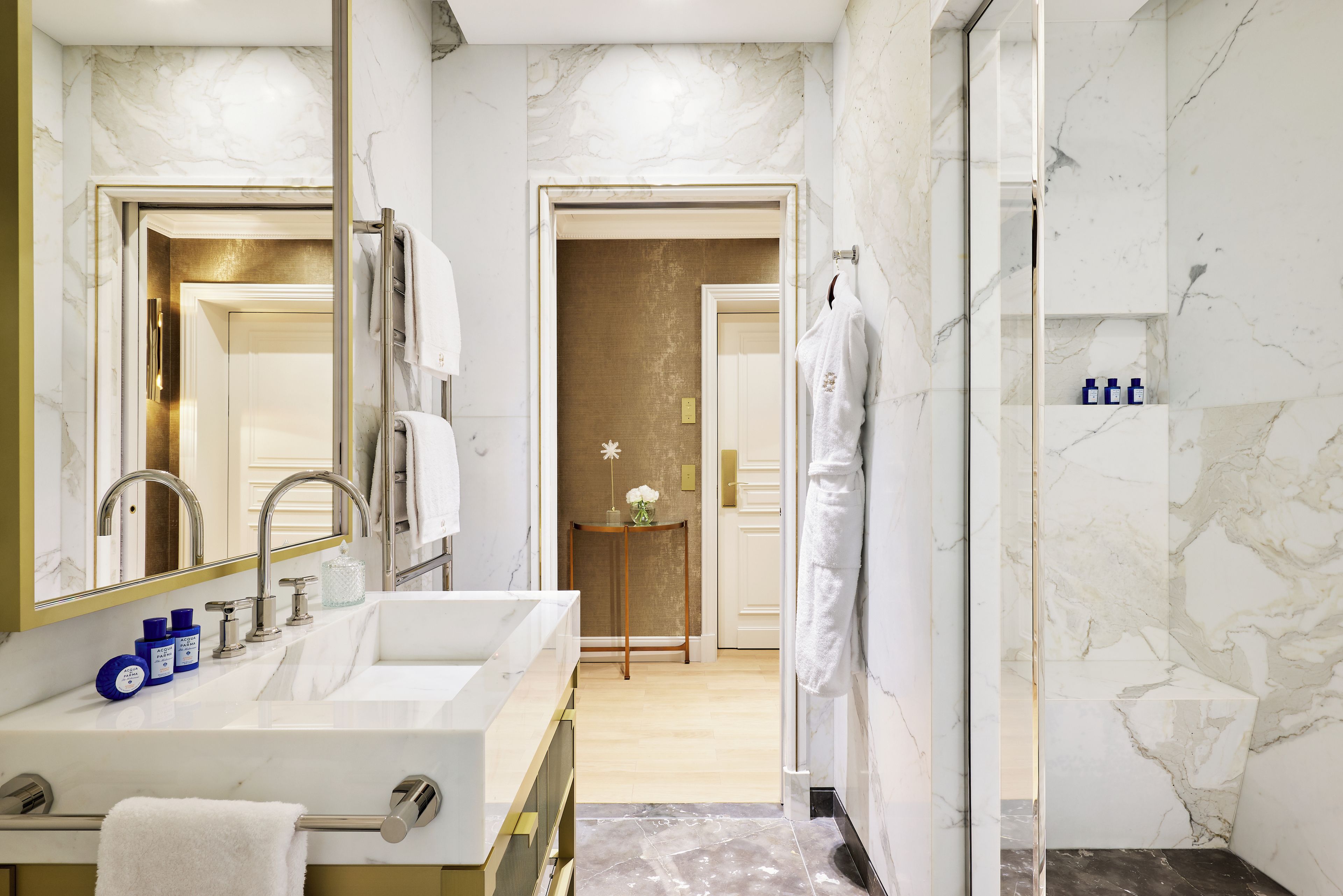 Un baño moderno con un espejo grande, un lavamanos blanco con detalles dorados y una zona de ducha.
