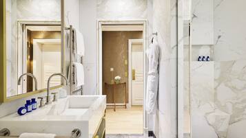 Un baño moderno con un espejo grande, un lavamanos blanco con detalles dorados y una zona de ducha.