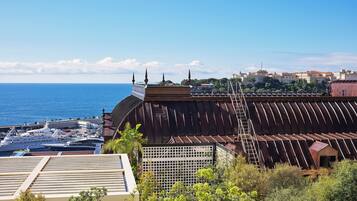 A coastal building with a sloped roof, a staircase, and a view of the sea and distant buildings.