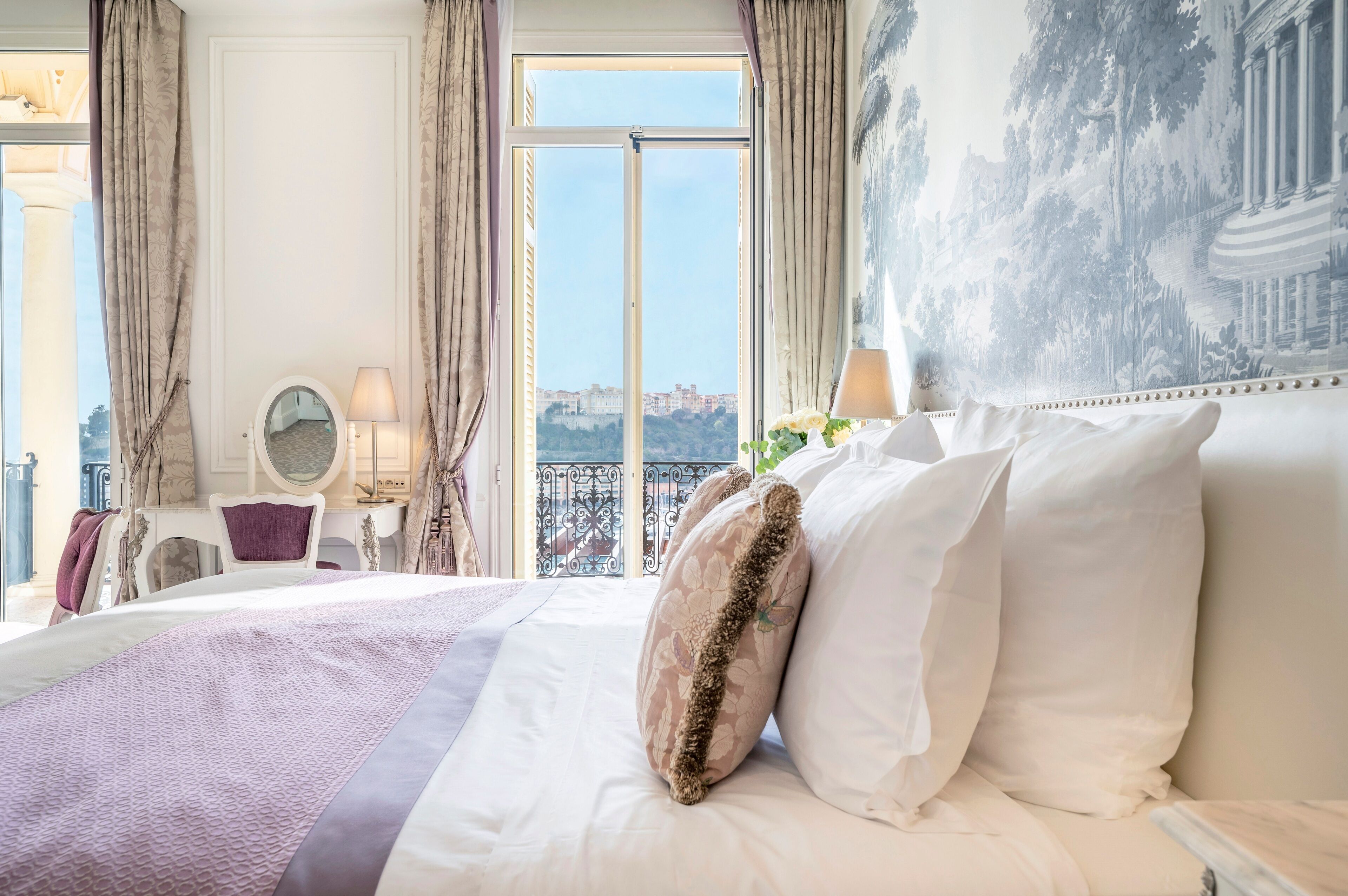 A hotel room with a large bed, a view of the city, and a decorative mirror.
