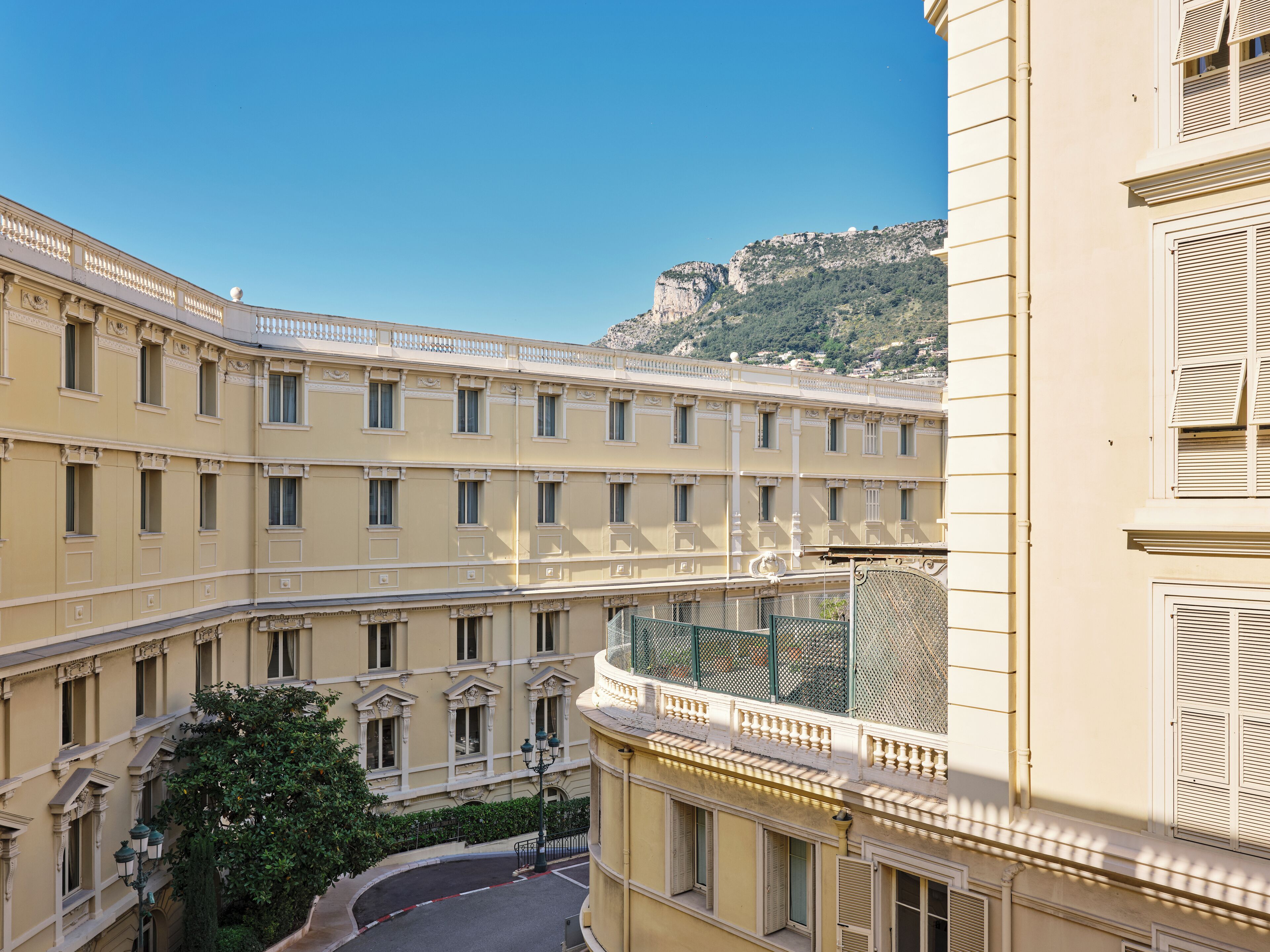 Un immeuble à plusieurs étages doté d’un balcon incurvé, une rue en contrebas et une montagne en arrière-plan.