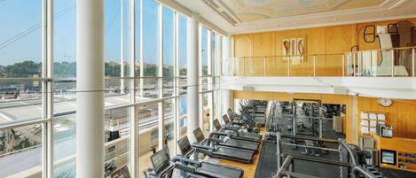 A gym with multiple treadmills, weight machines, and a view of the city through large windows.